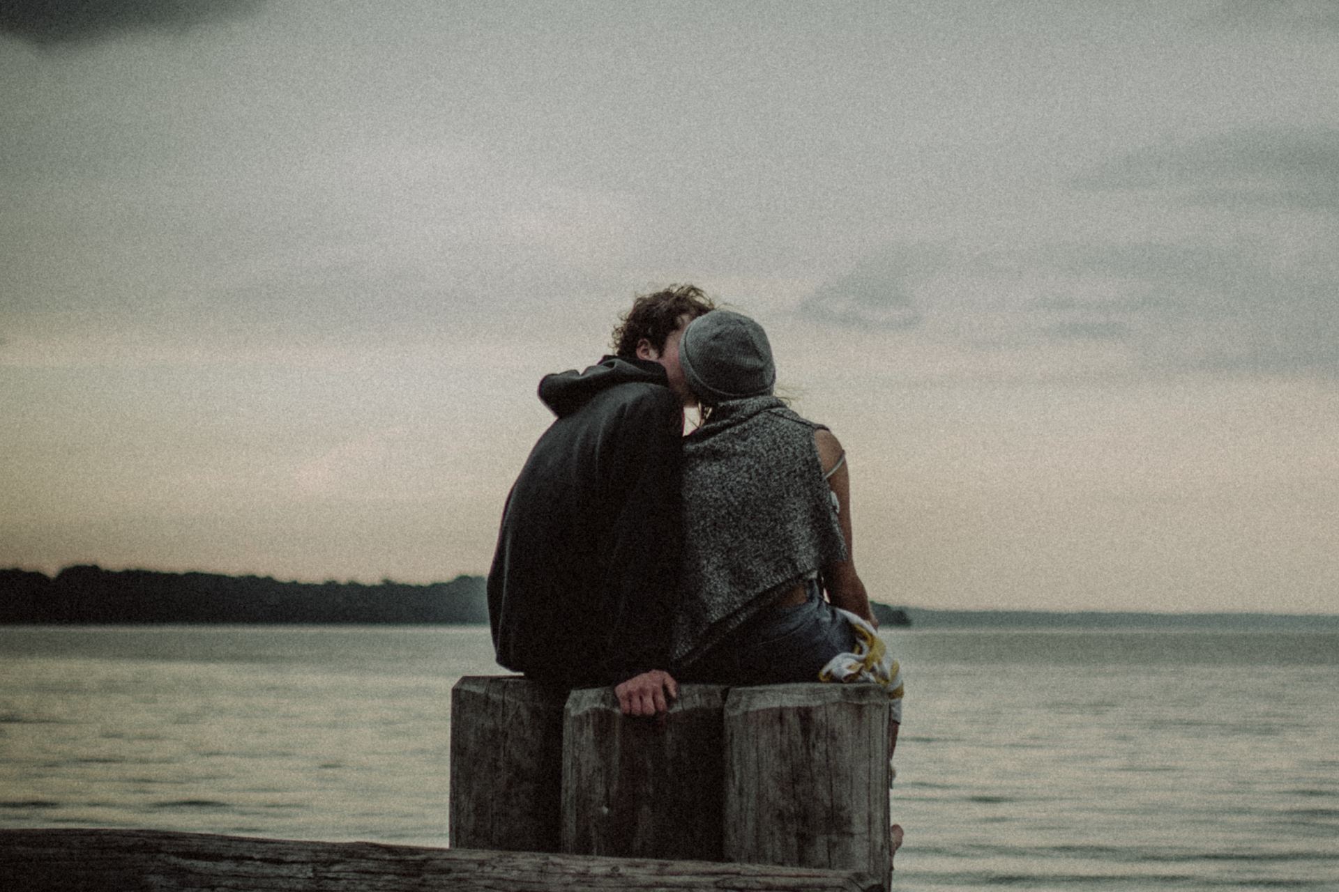 man and woman sitting and kissing on post near the body of water