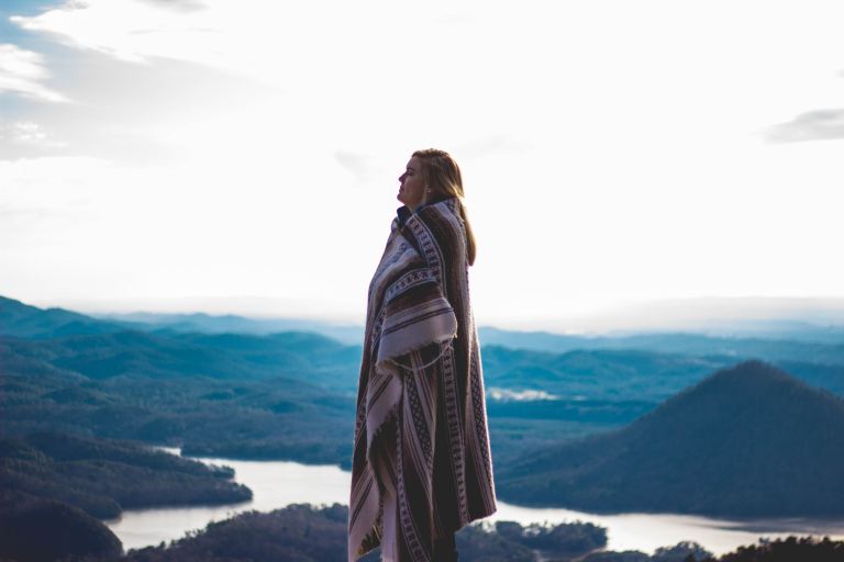 woman wearing coat standing on cliff