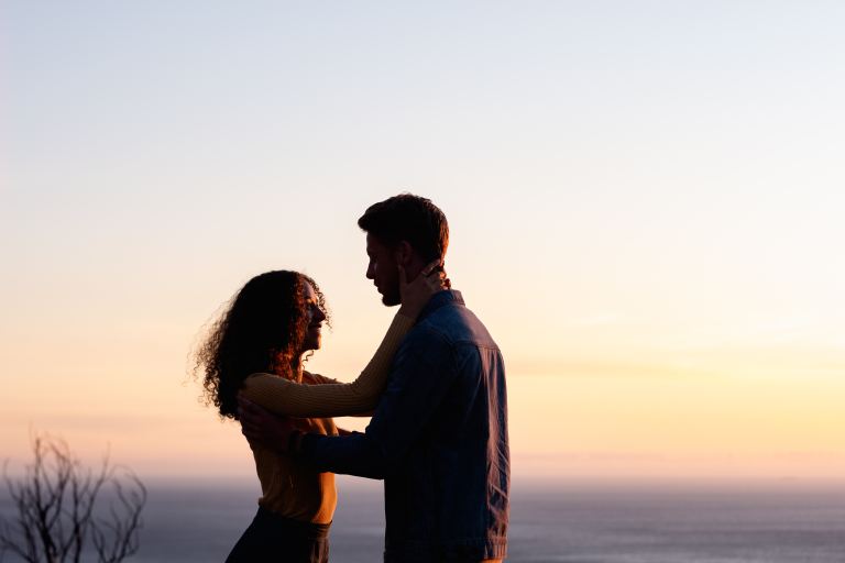 man and woman standing near body of water during sunset