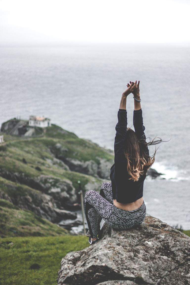 woman sitting on stone formation near cliff during daytime