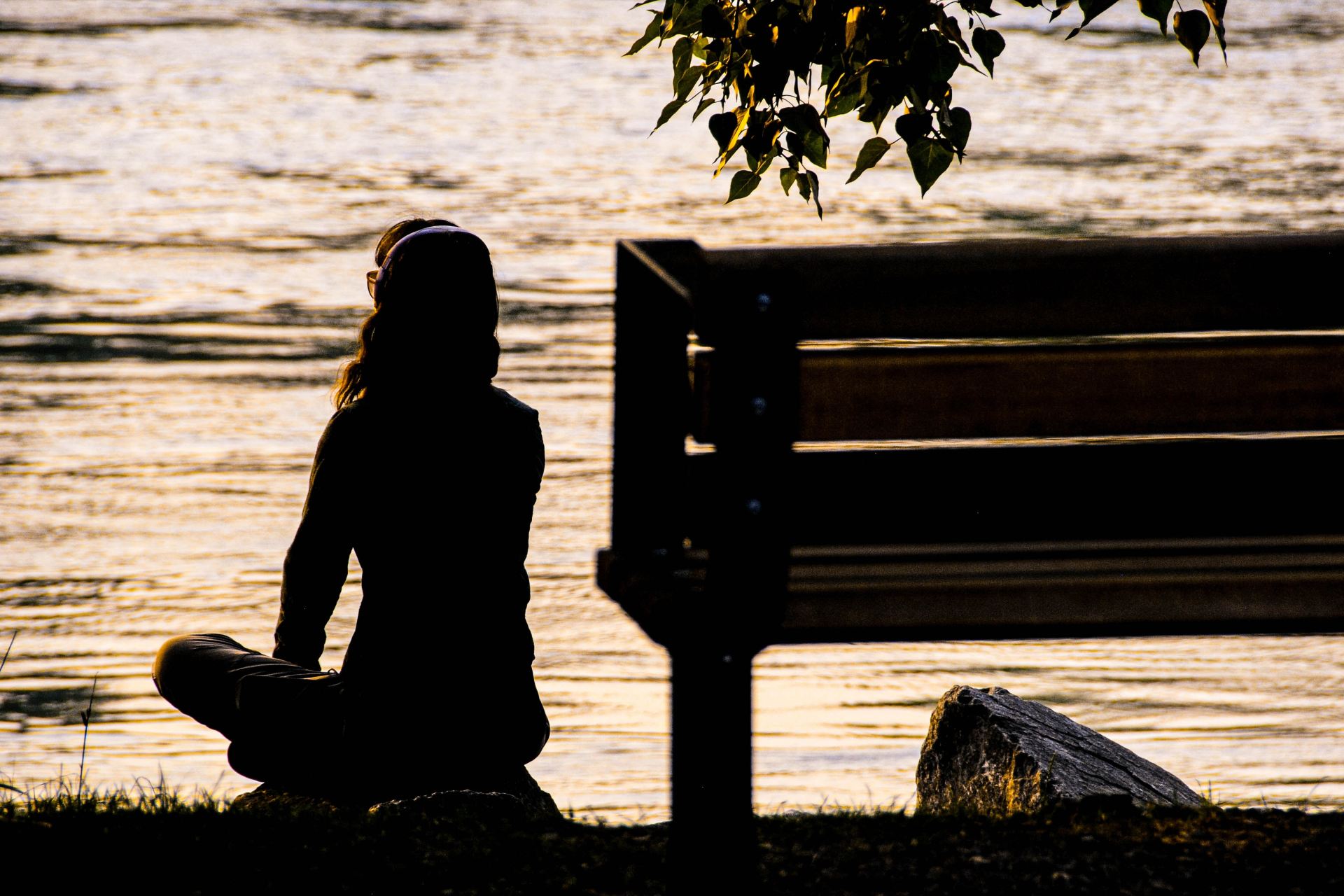 silhouette of person sitting on bench near body of water during daytime