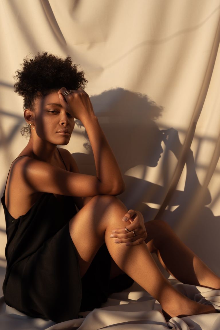 woman wearing black spaghetti strap dress sitting while touching her forehead