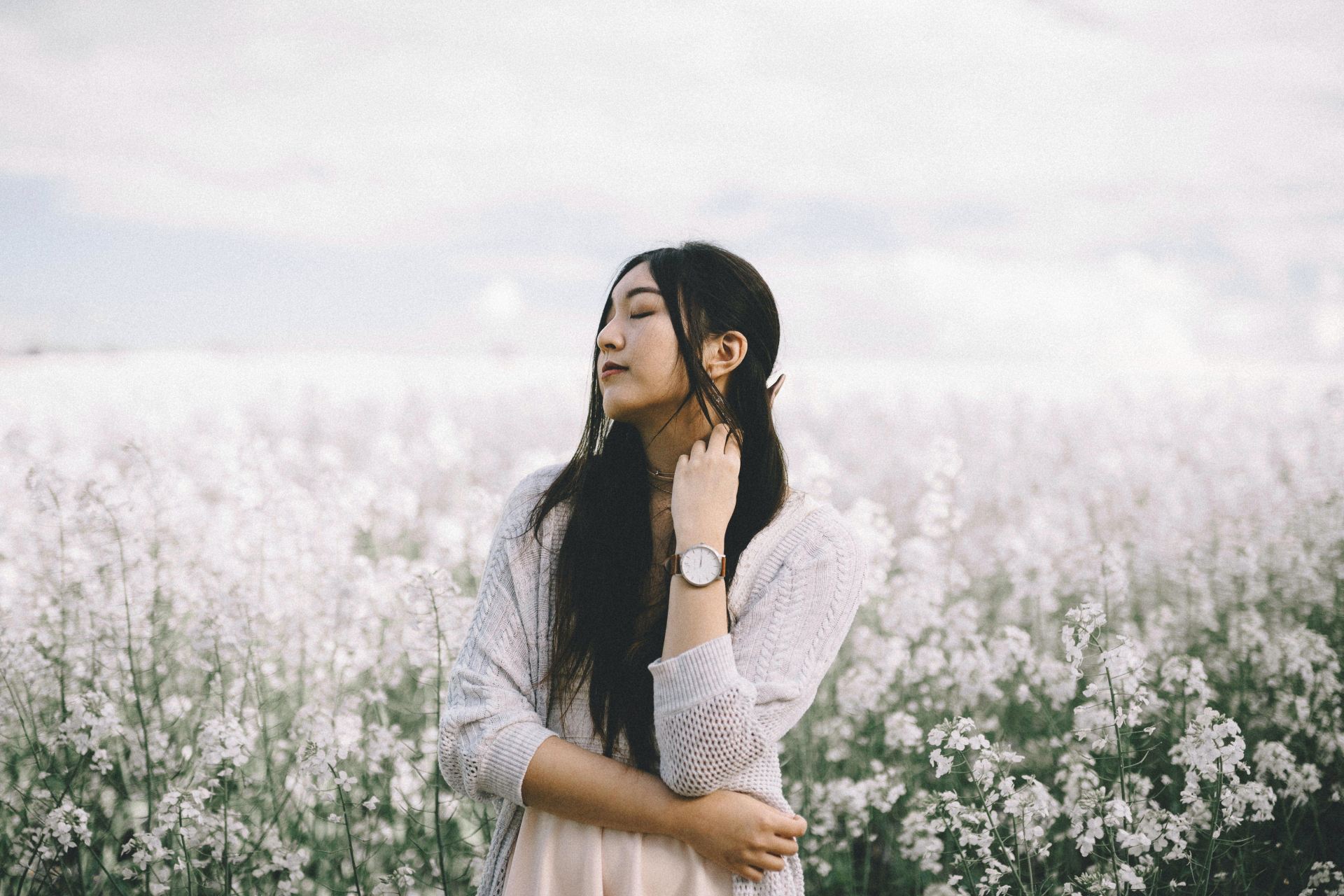 woman wearing peach inner top with gray knitted cardigan standing behind white flowerfield during daytime photography