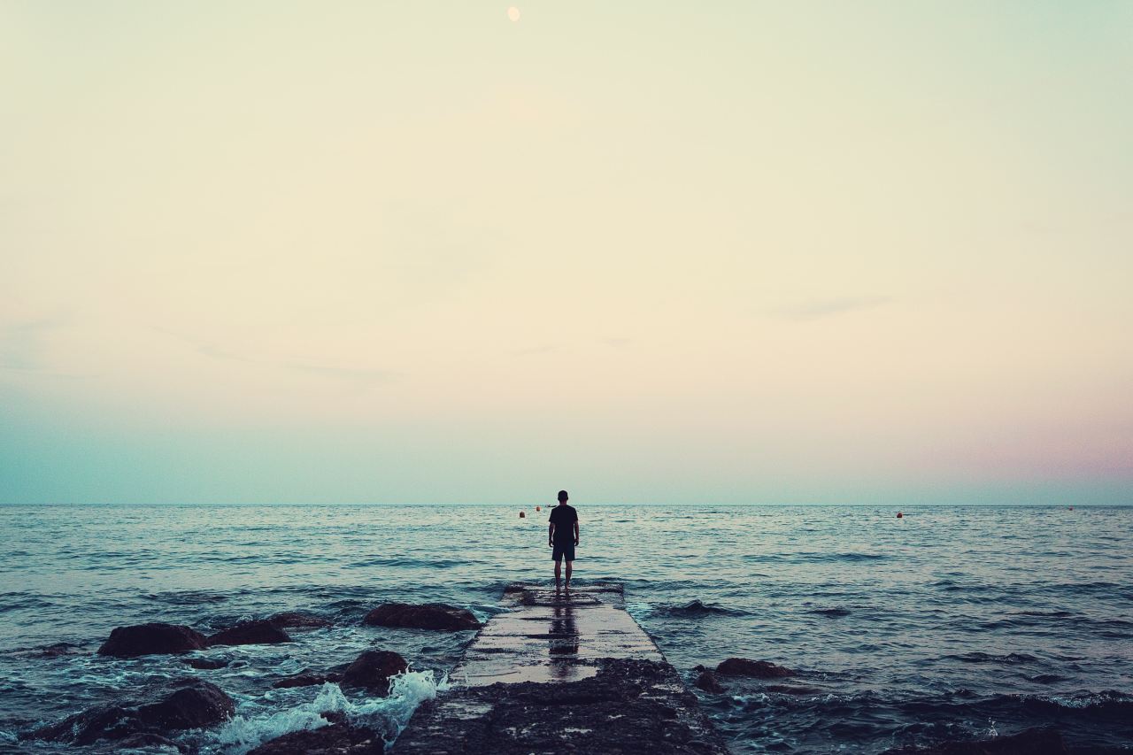 silhouette of person standing on sea dock under cloudy sky