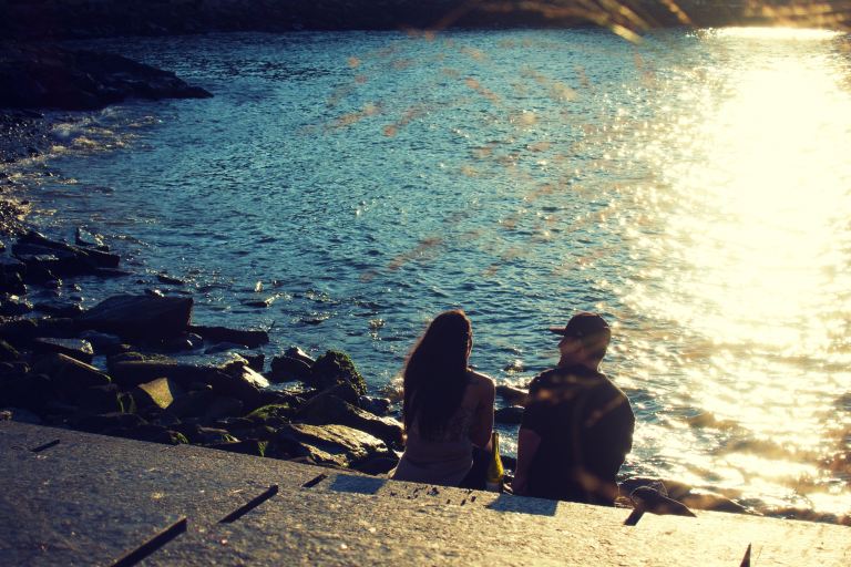 silhouette of people sitting on rock near body of water during daytime