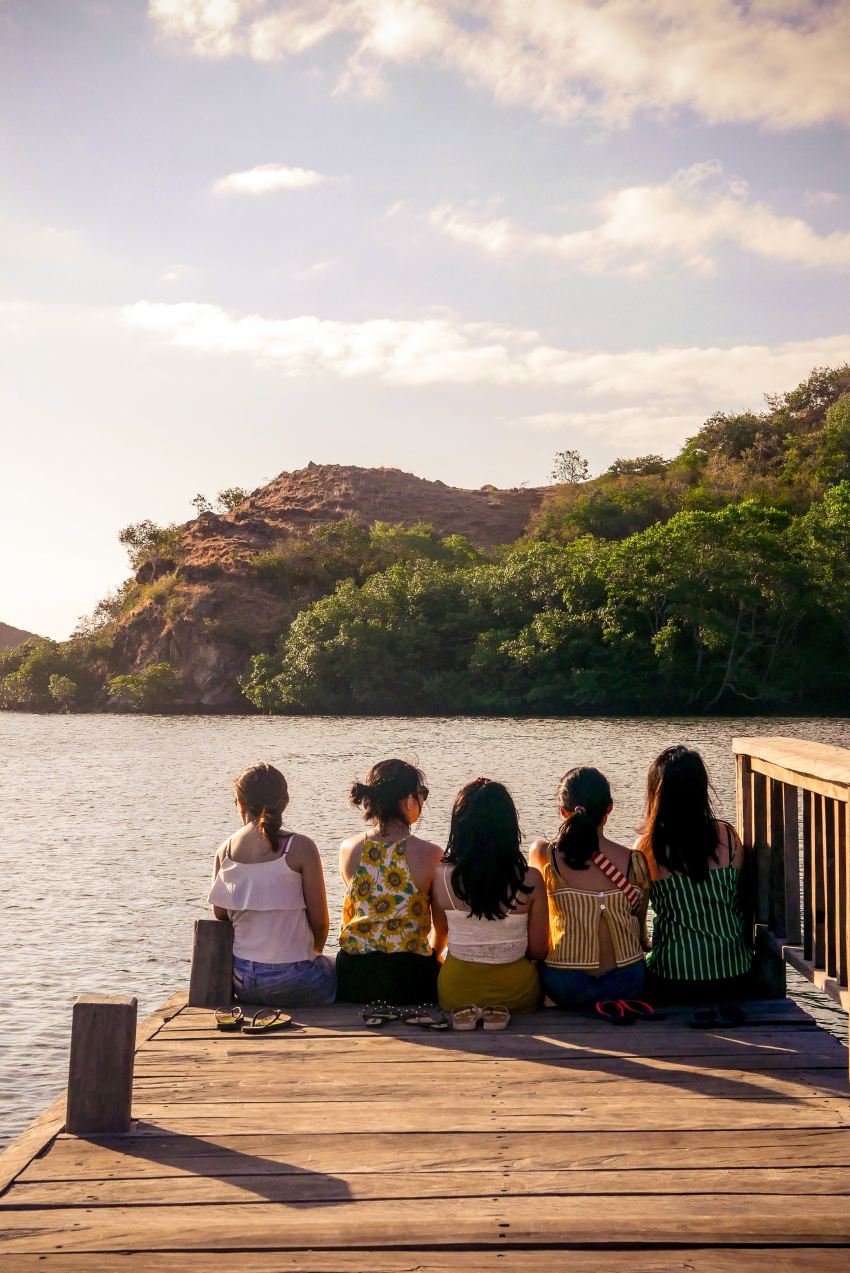 group of people sitting on brown wooden bench near body of water during daytime