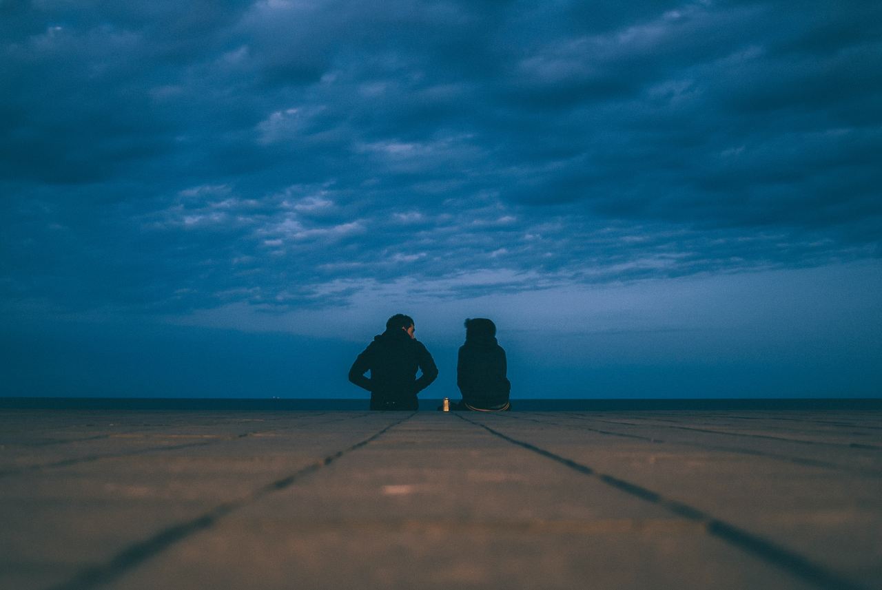 two people wearing black jackets sitting on floor