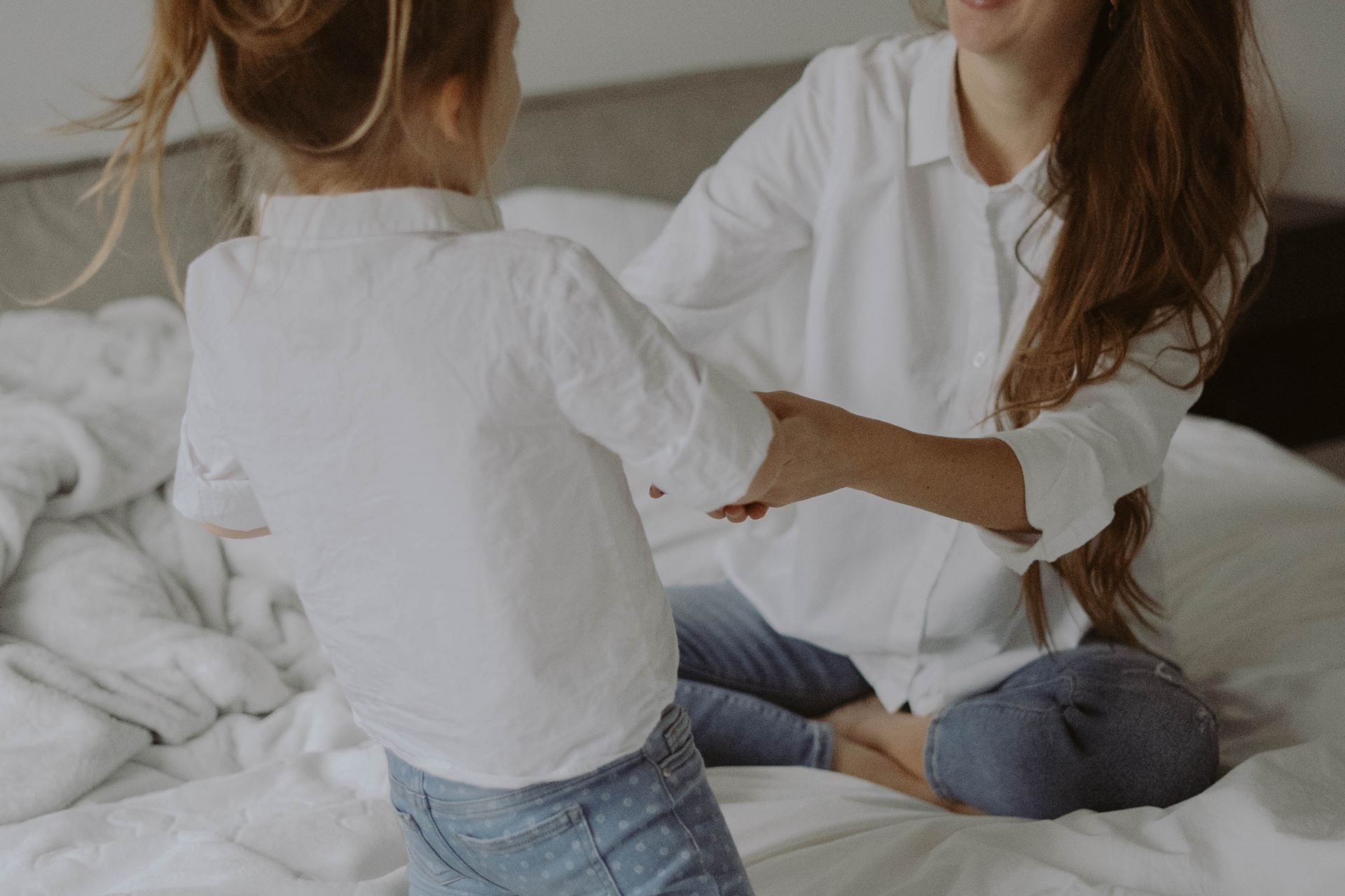 woman in white long sleeve shirt and blue denim jeans sitting on bed