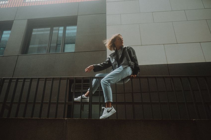 woman in black jacket and blue denim jeans sitting on black metal railings