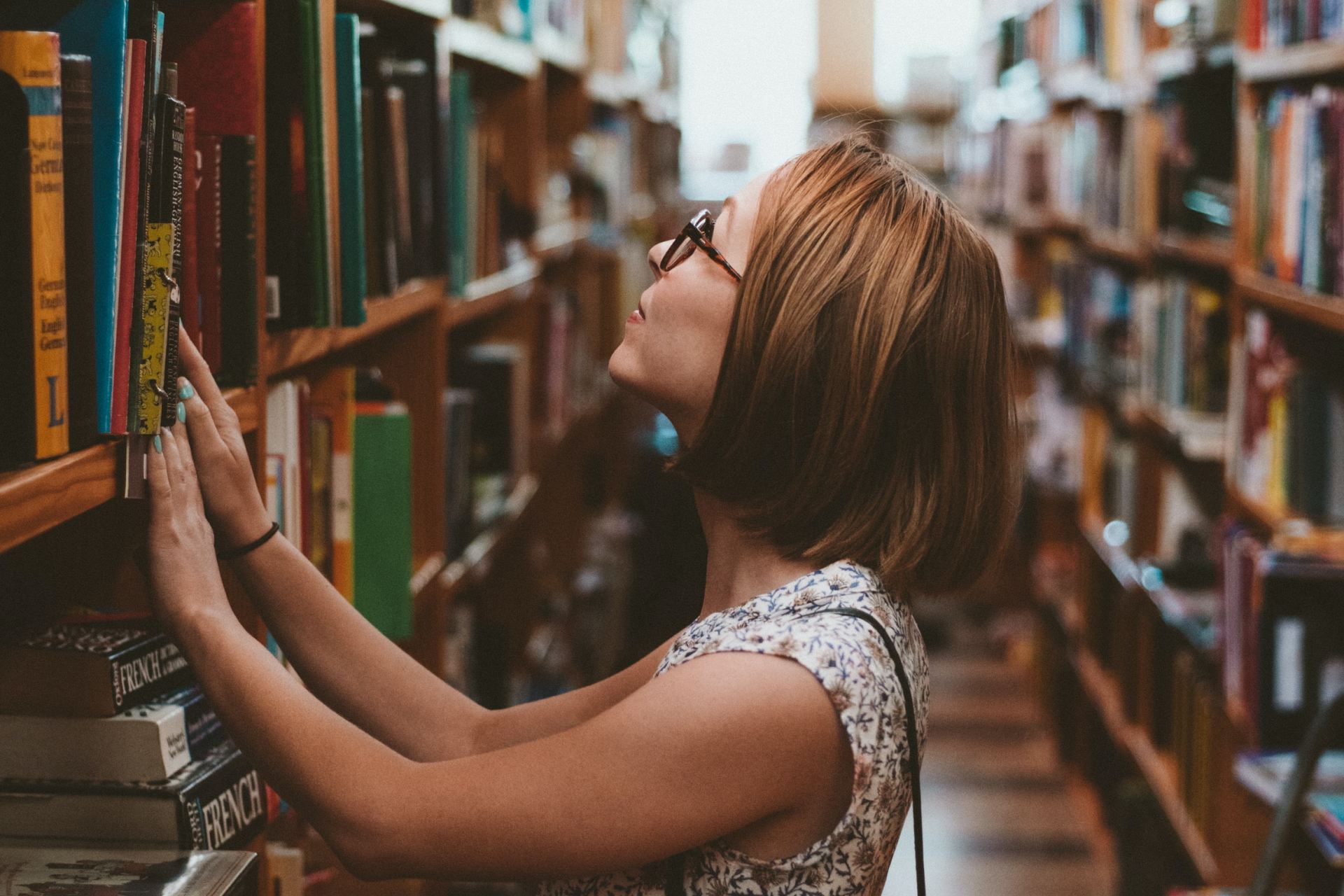 woman standing between library book shelves