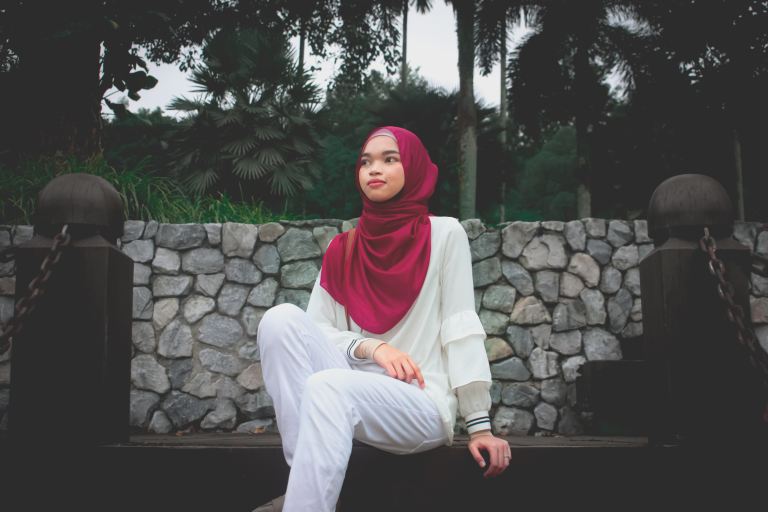 woman in white long sleeve shirt and red hijab sitting on brown wooden bench