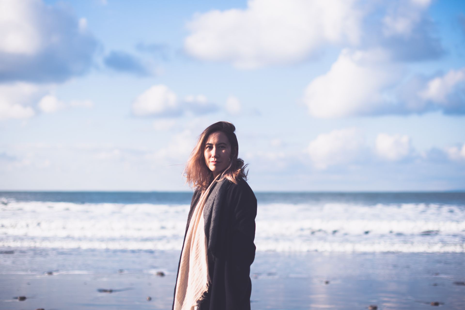 woman in black coat standing on beach during daytime