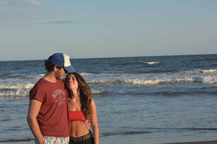 woman in red shirt and blue denim daisy dukes standing on beach shore during daytime