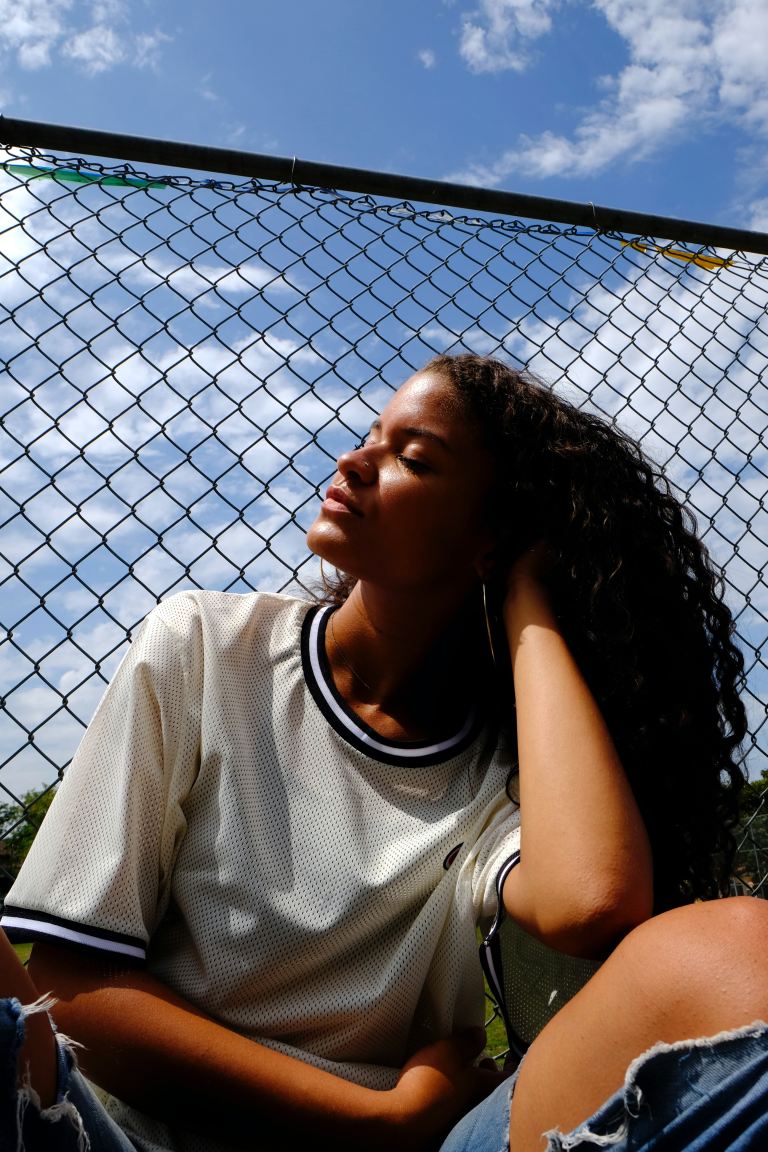 woman in white crew neck t-shirt leaning on chain link fence