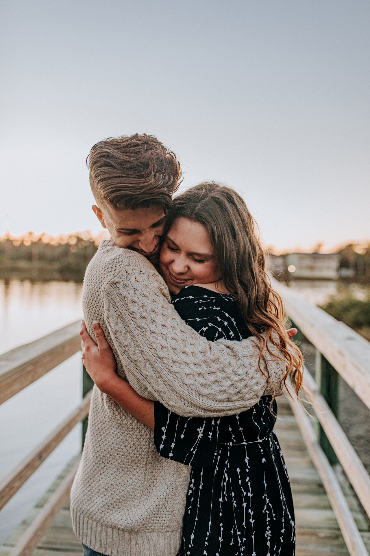 smiling man and woman hugging each other on wooden bridge during day