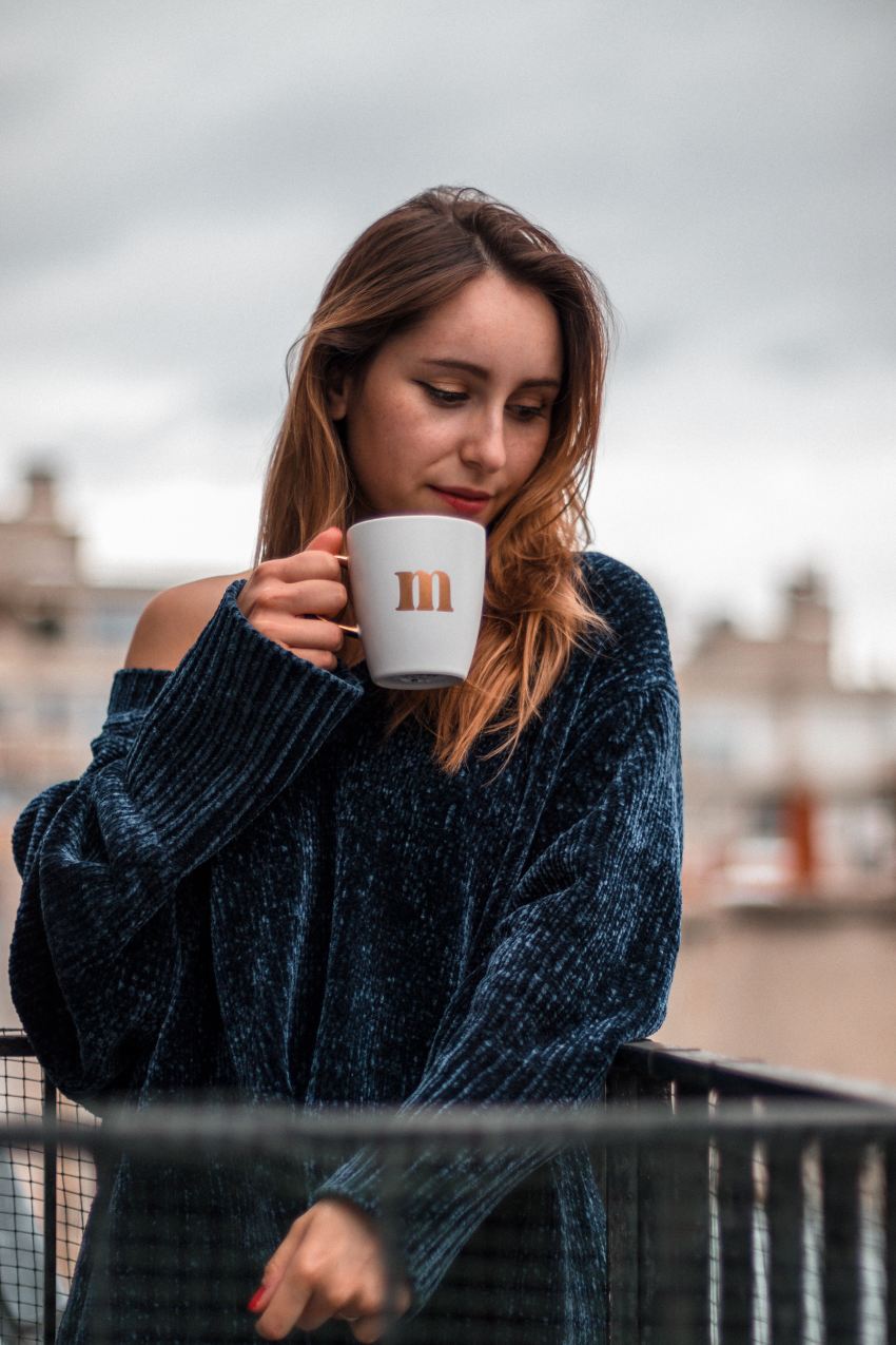 woman in blue sweater holding white ceramic mug