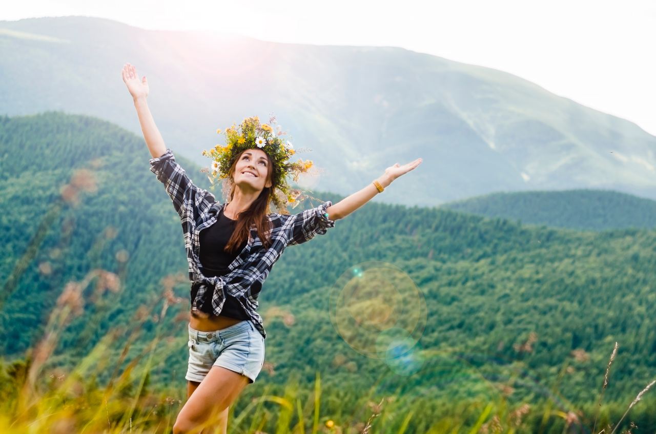 woman raising hands behind mountain covered by trees