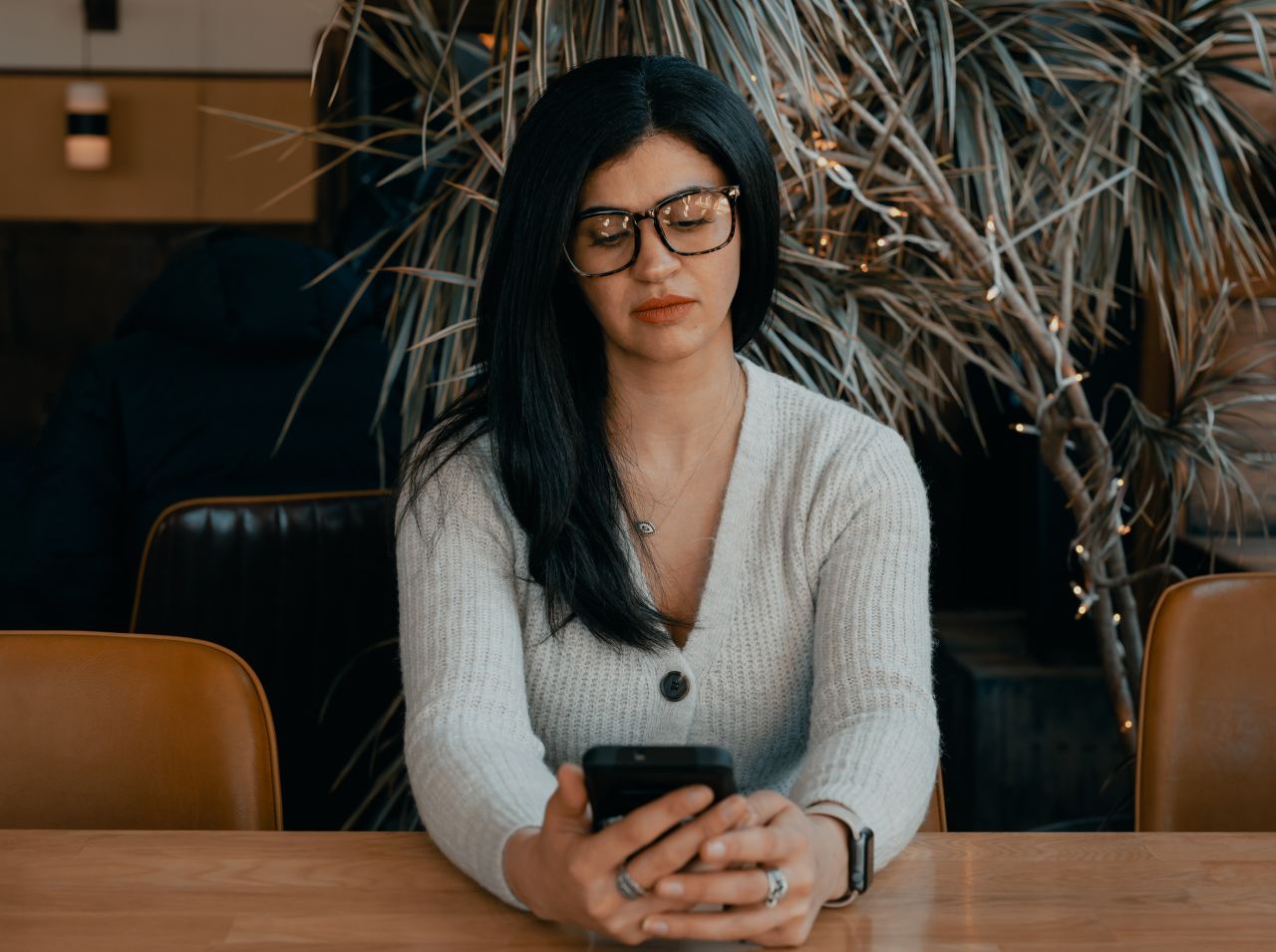 woman in white cardigan holding black smartphone