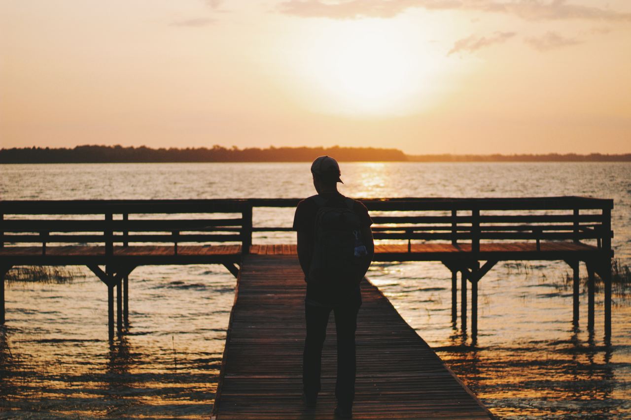 silhouette of man walking on dock during golden hour