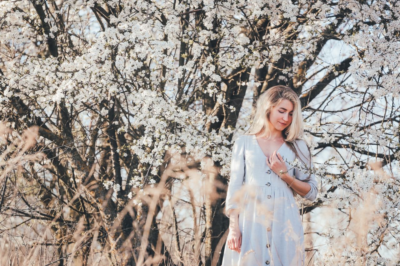 woman in white sleeveless dress standing under white cherry blossom tree during daytime