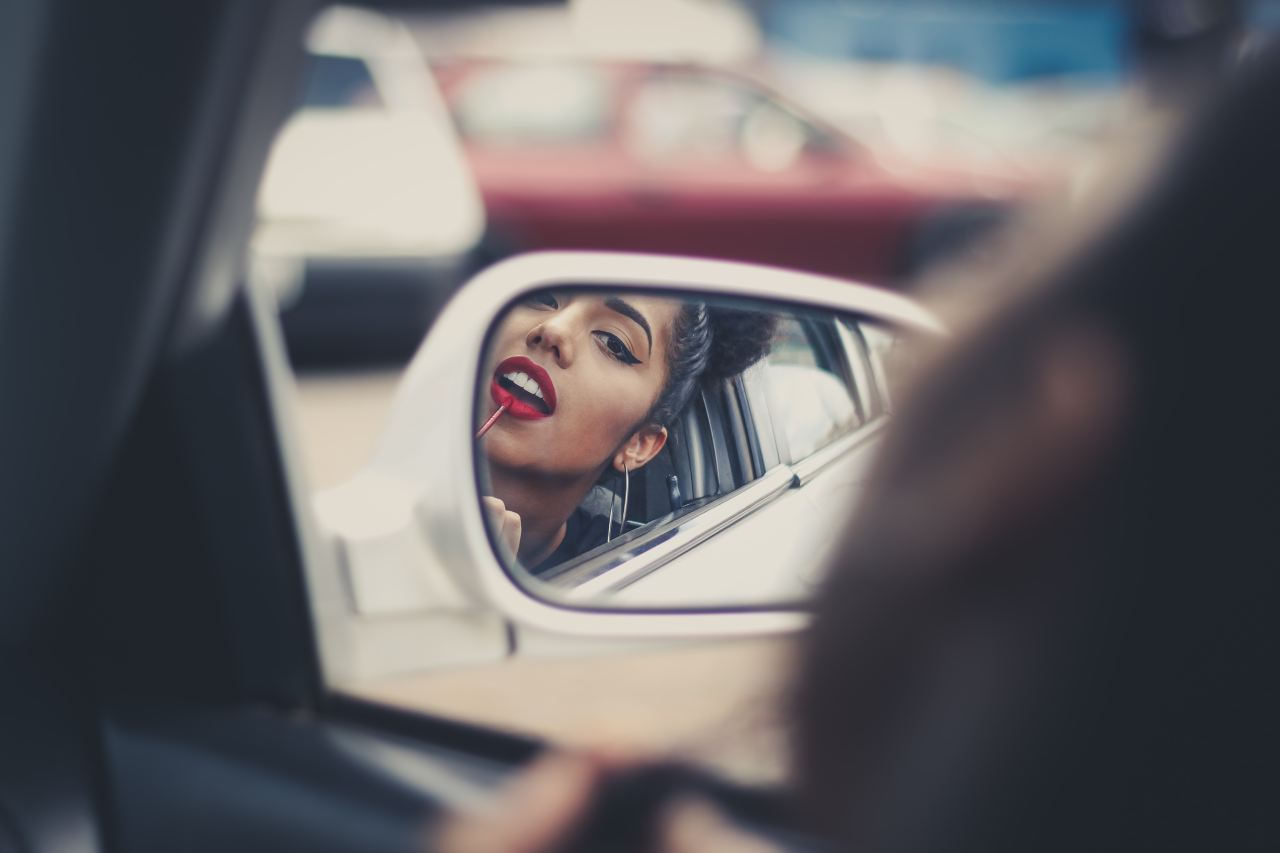 woman putting liquid lipstick on her lips while looking at vehicle's mirror during daytime