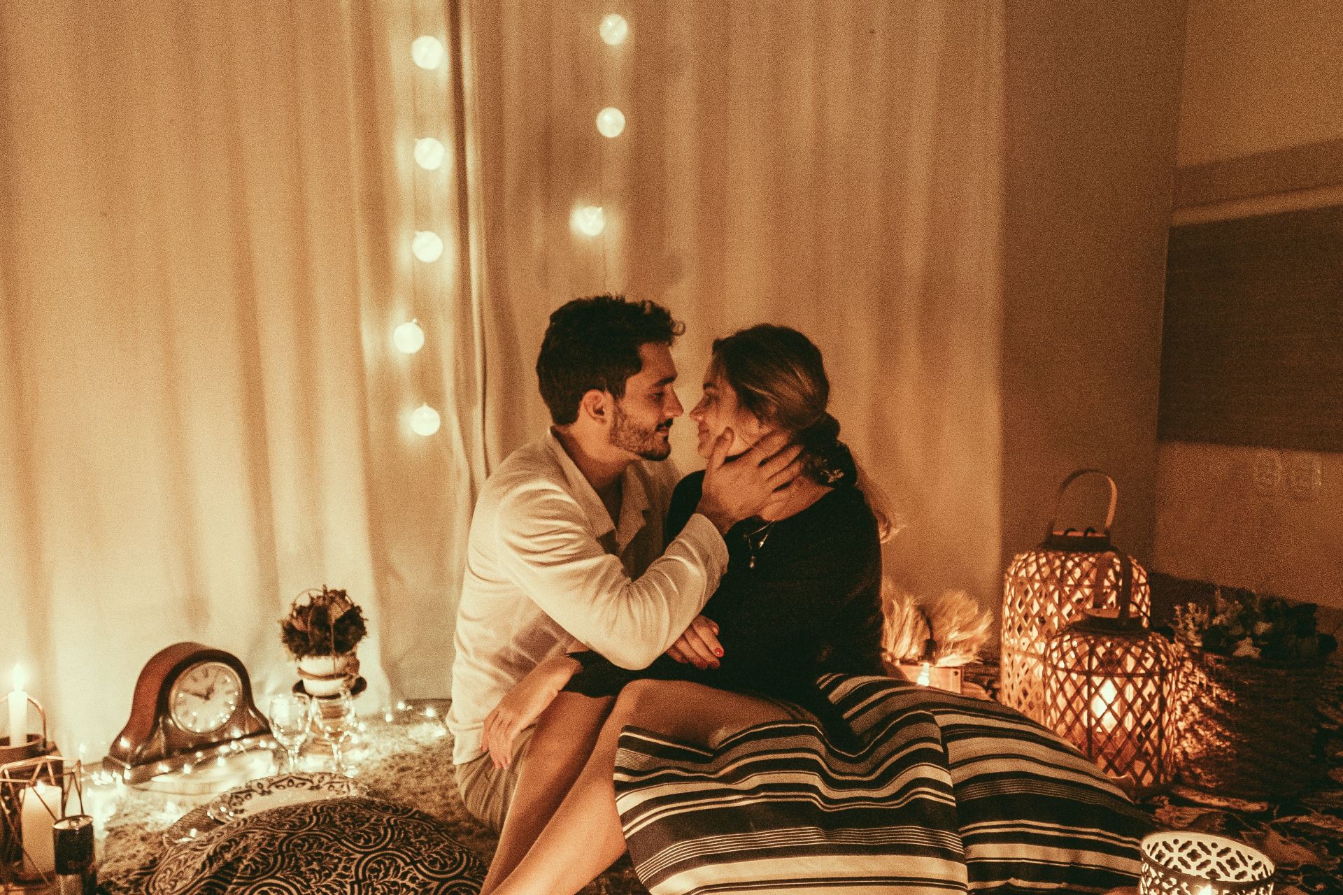 man and woman sitting on floor and about to kiss with lighted candles inside room