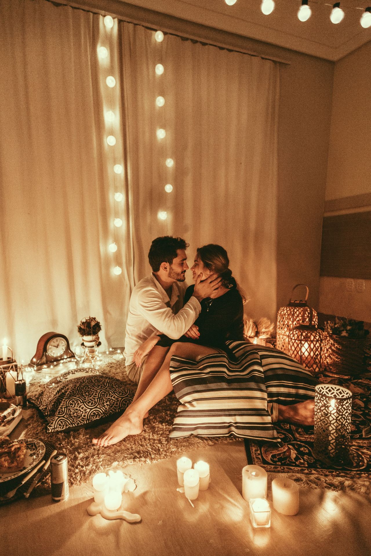 man and woman sitting on floor and about to kiss with lighted candles inside room