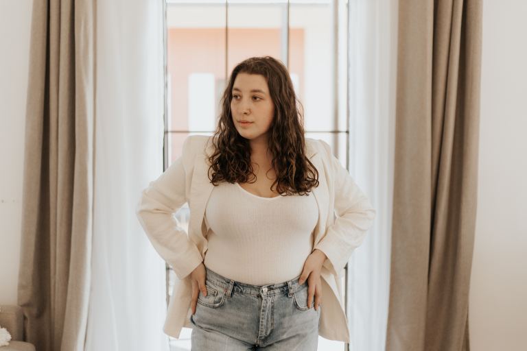 woman in white long sleeve shirt and blue denim jeans standing near window