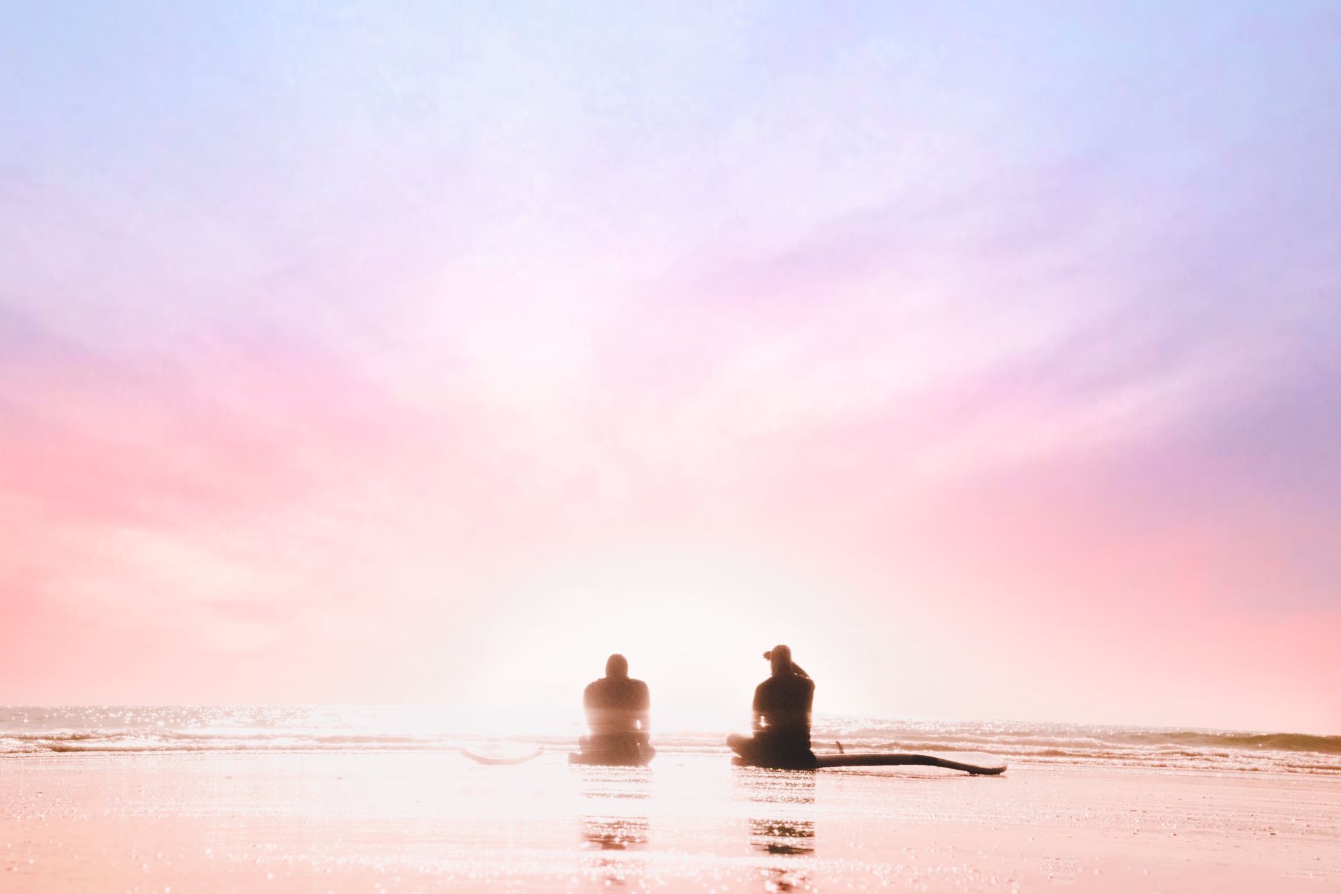 silhouette of two person sitting on seashore during dawn