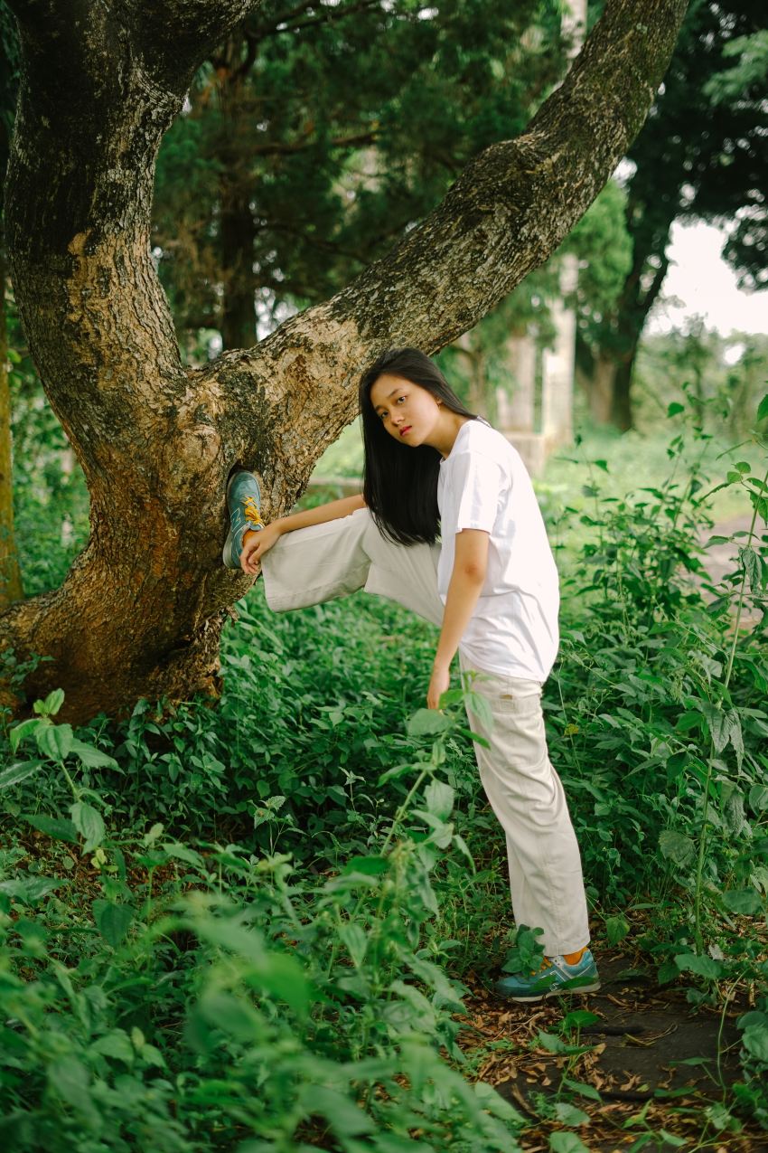 woman in white shirt and white pants standing beside tree