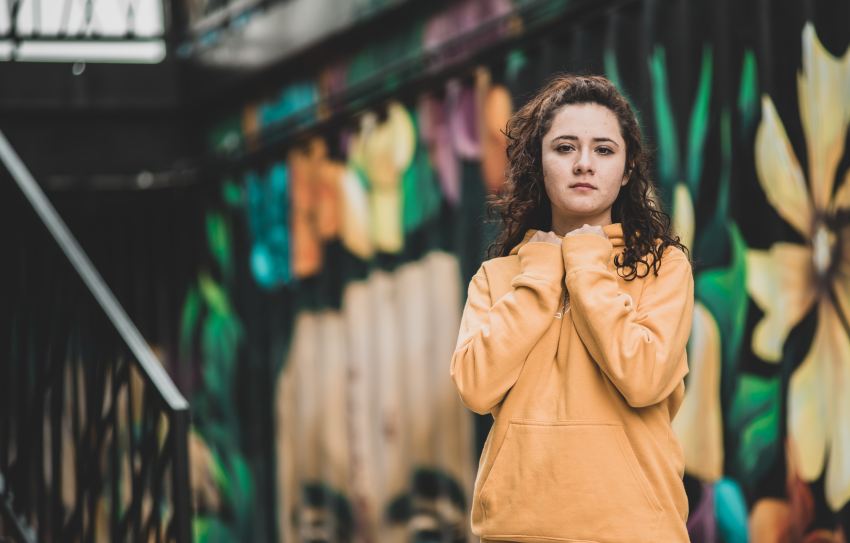 woman in brown coat standing near graffiti wall during daytime