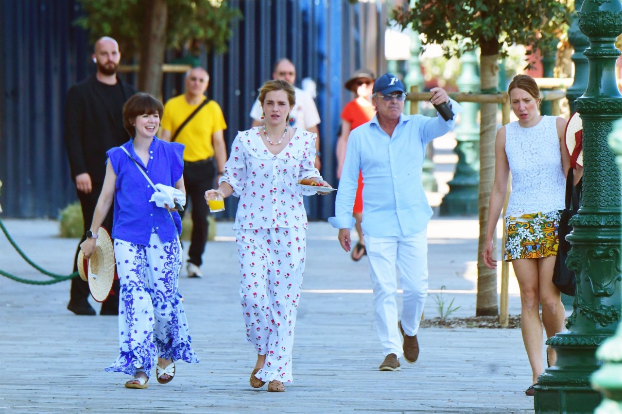 Emma Watson in a cherry-printed outfit and red cherry drop earrings carrying a breakfast plate alongside a friend in Venice.