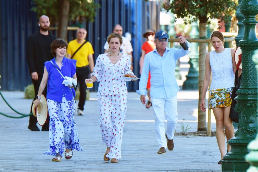 Emma Watson in a cherry-printed outfit and red cherry drop earrings carrying a breakfast plate alongside a friend in Venice.