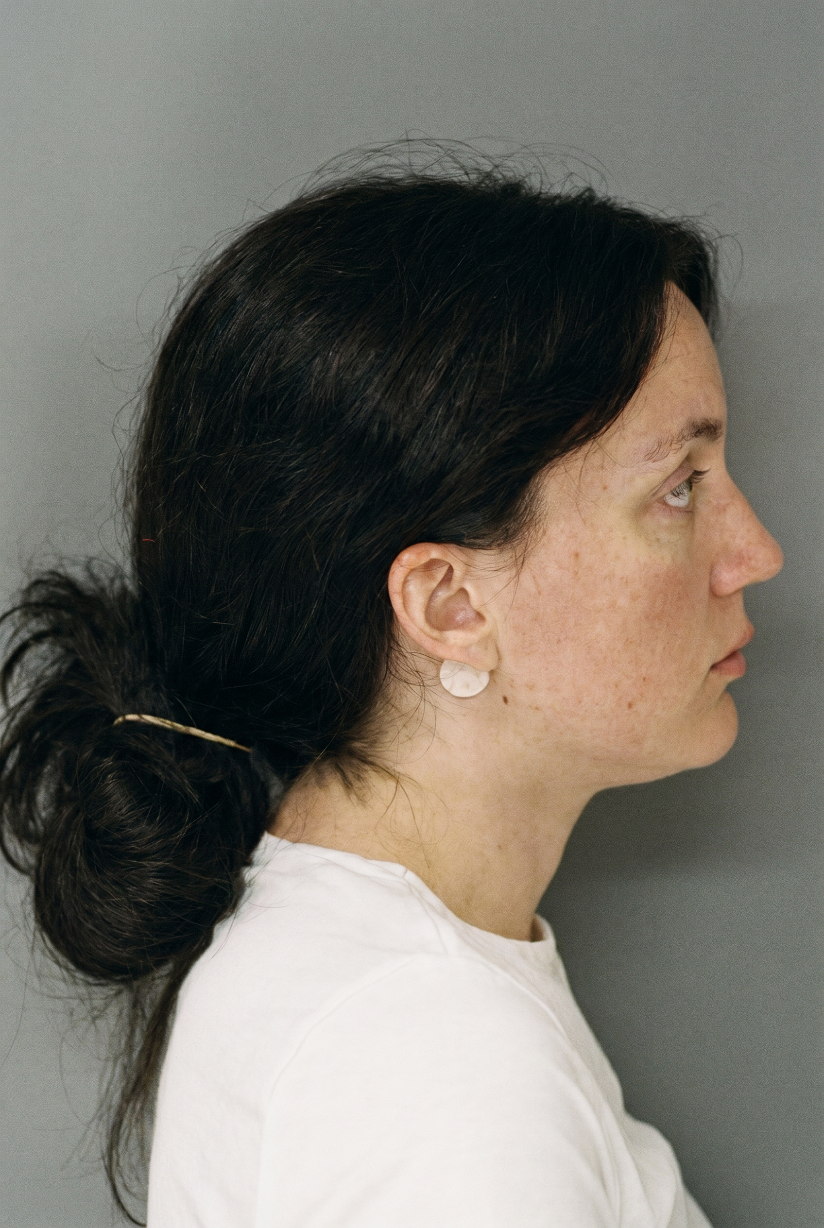 Click to open the image gallery Side profile of a dark-haired woman in a white top wearing a circular earring, against a gray background.
