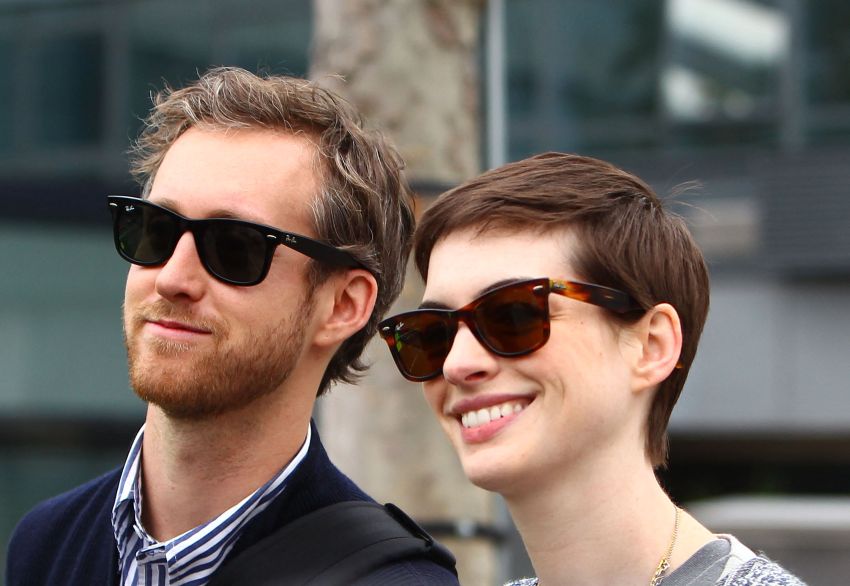 A man and short-haired woman wearing matching Ray-Ban sunglasses pose together outdoors, smiling.