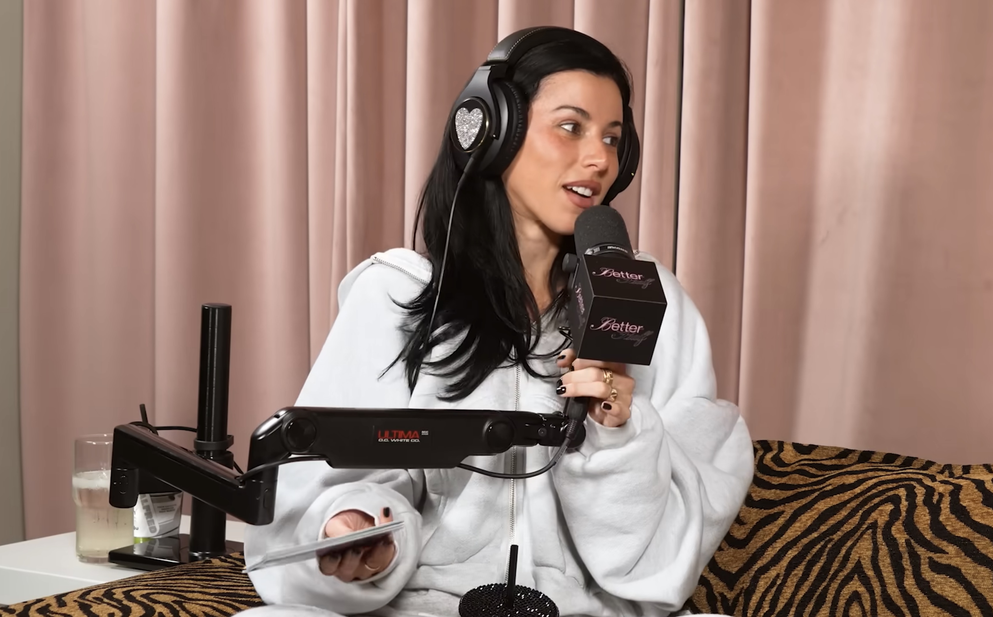 Click to open the image gallery Victoria Villarroel in a white hoodie and bejeweled headphones holding a podcast microphone labeled "Better Half."
