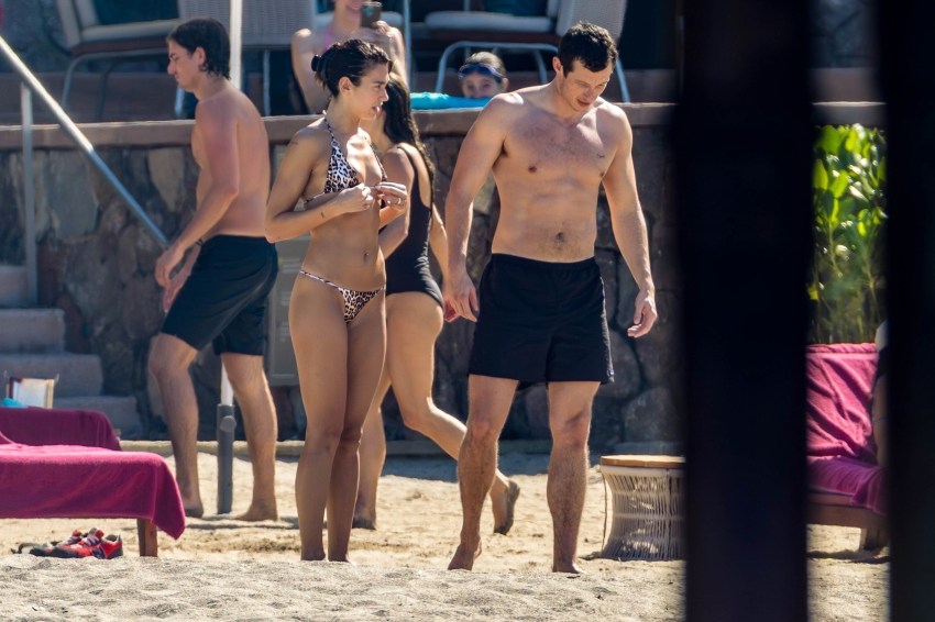 Dua Lipa in an animal print bikini relaxing on a beach lounge chair while Callum Turner rubs sunscreen on her back in Mexico