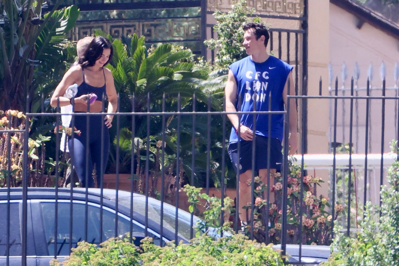 A dark-haired woman in navy workout gear and a man in a blue CFC London sleeveless shirt walk together laughing outside a gated property.