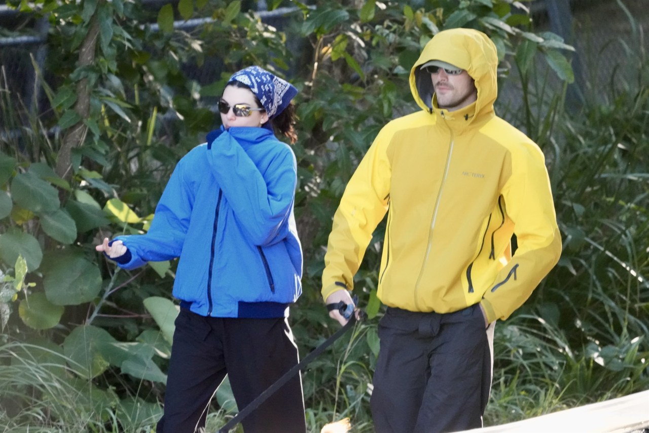 A woman in a blue jacket and blue bandana and a man in a yellow Arc'teryx hooded jacket walk together outdoors in Byron Bay, Australia.