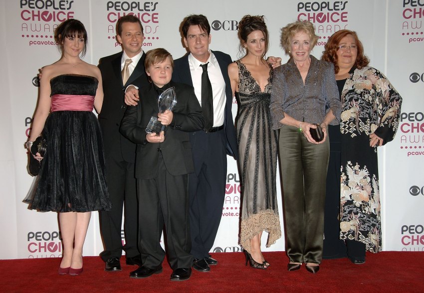 Seven TV cast members posed together on a red carpet in front of a People's Choice Awards backdrop, one boy holding a crystal award trophy.