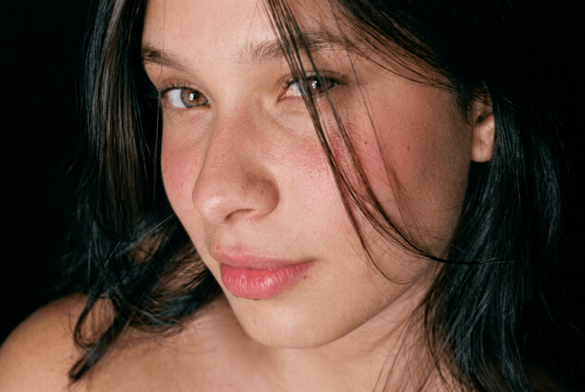 Close-up portrait of a young dark-haired woman with green eyes against a black background.