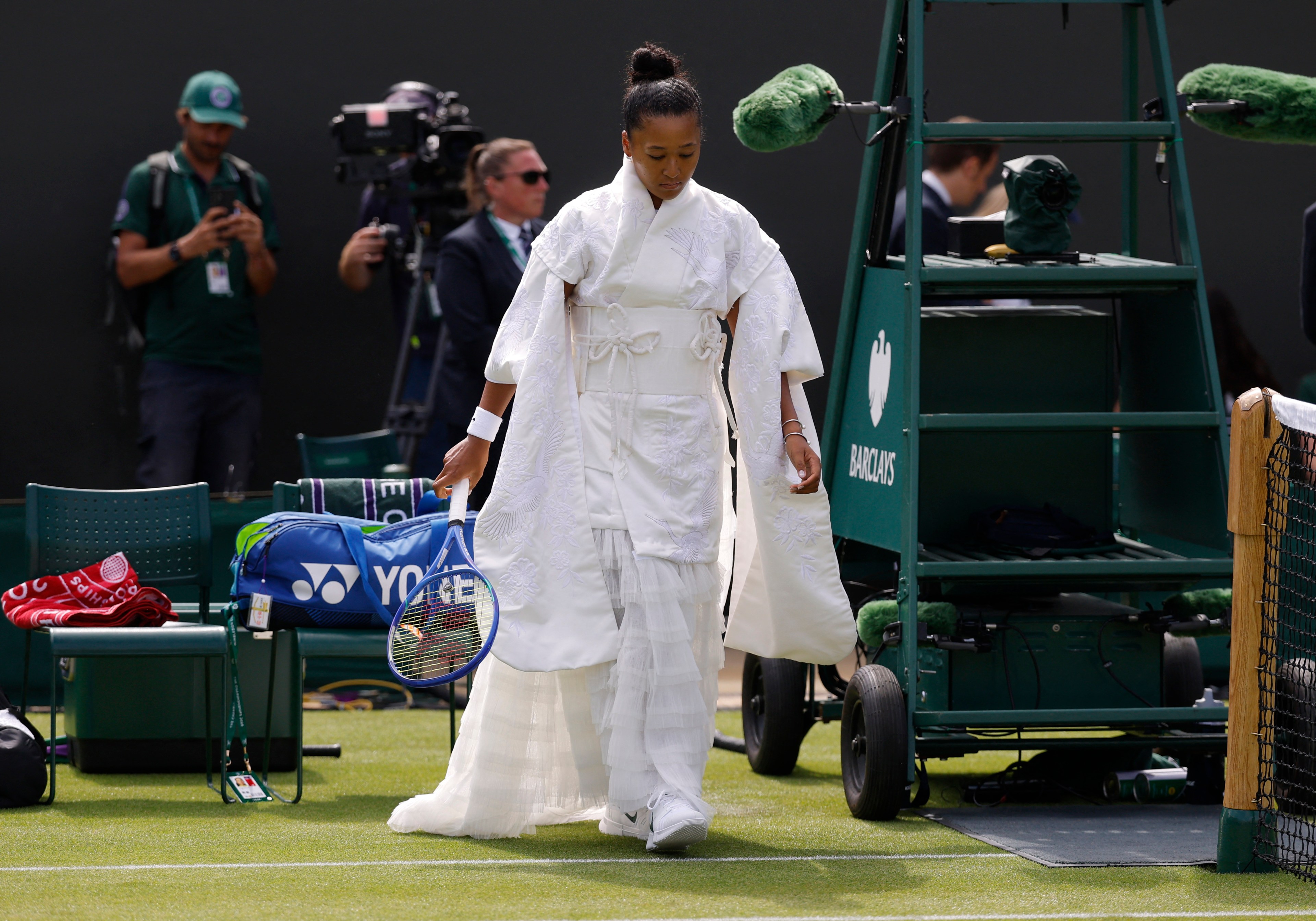 Naomi Osaka in a white kimono-inspired bridal gown holding a tennis racket on the Wimbledon grass court