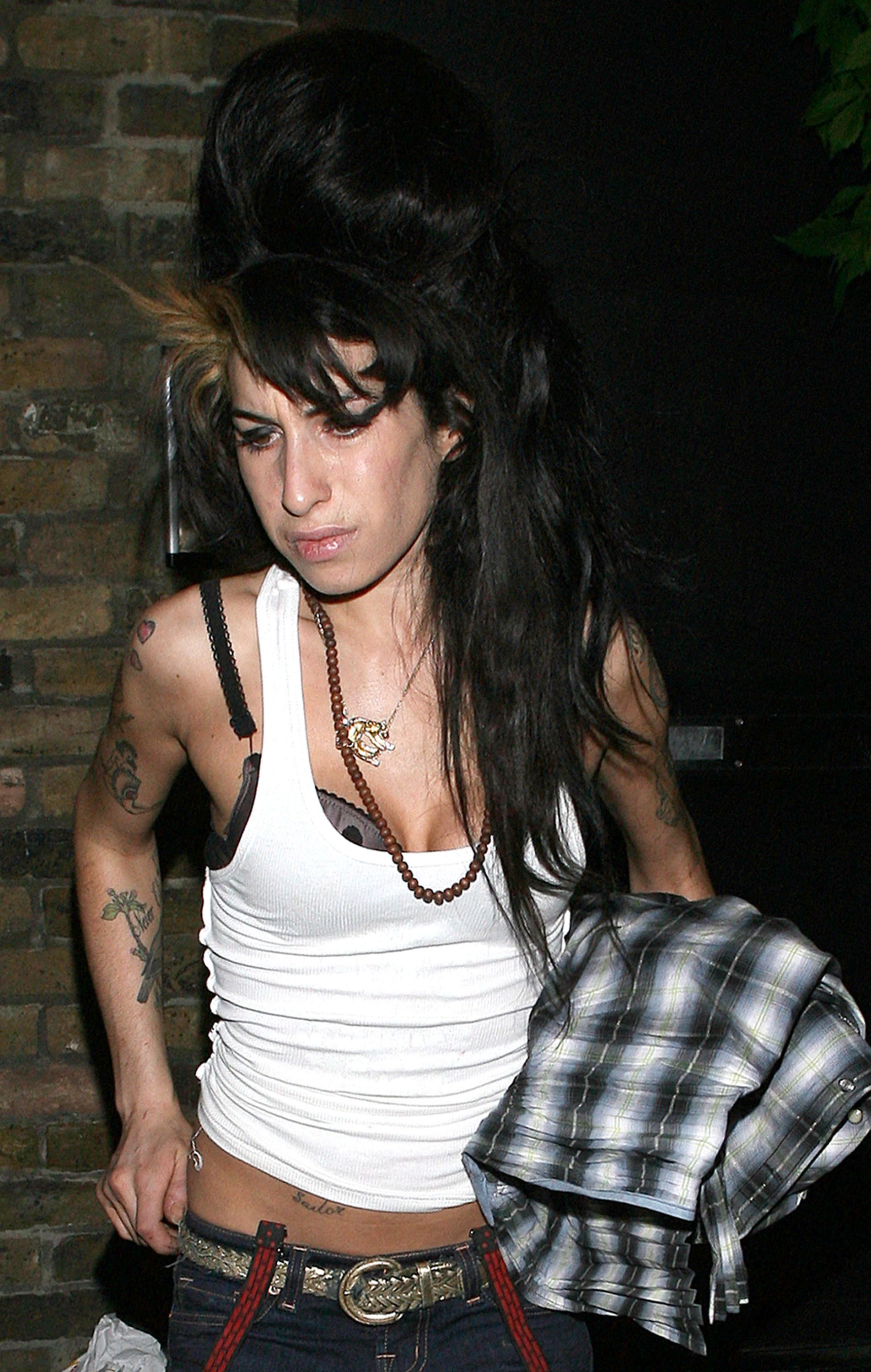Amy Winehouse outside her Camden home carrying bags, dressed in a white vest and blue jeans with black heels