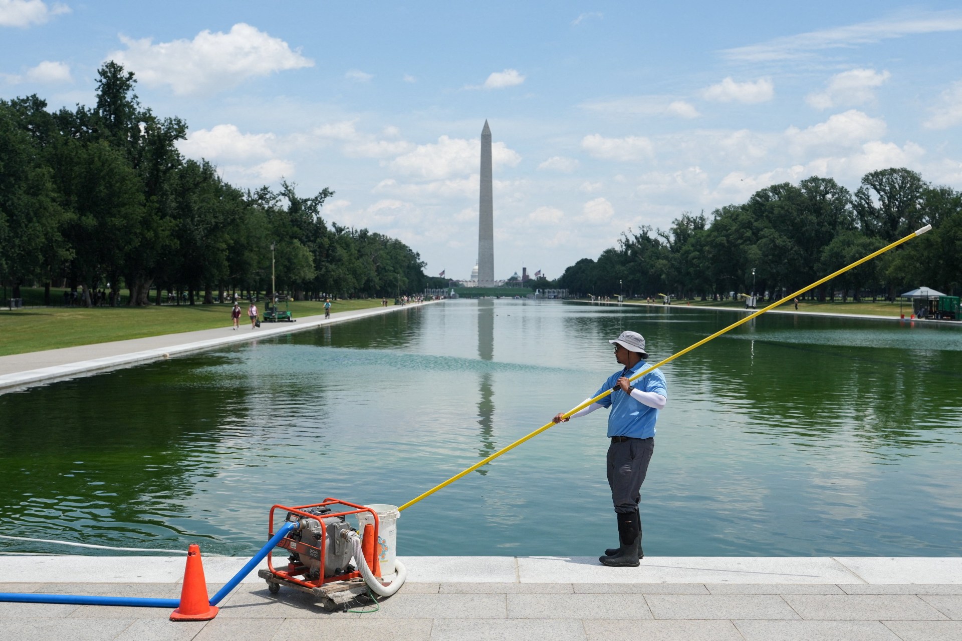 A worker clearing algae from the Lincoln Memorial Reflecting Pool, painted blue, in Washington, D.C.