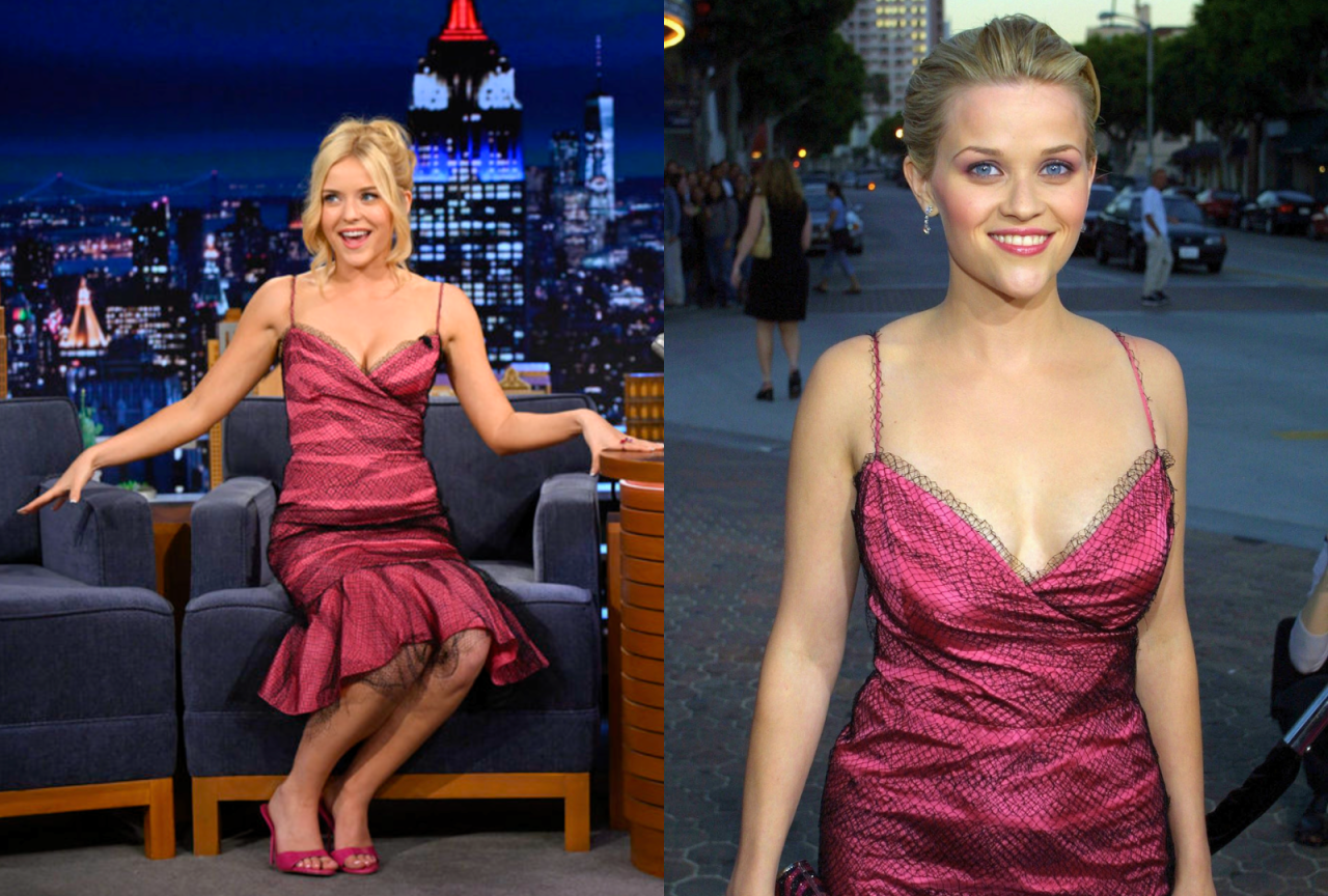 Blonde woman in a pink and black tulle spaghetti-strap dress sits in a guest chair on a late-night talk show set, leaning toward the host's wooden desk.