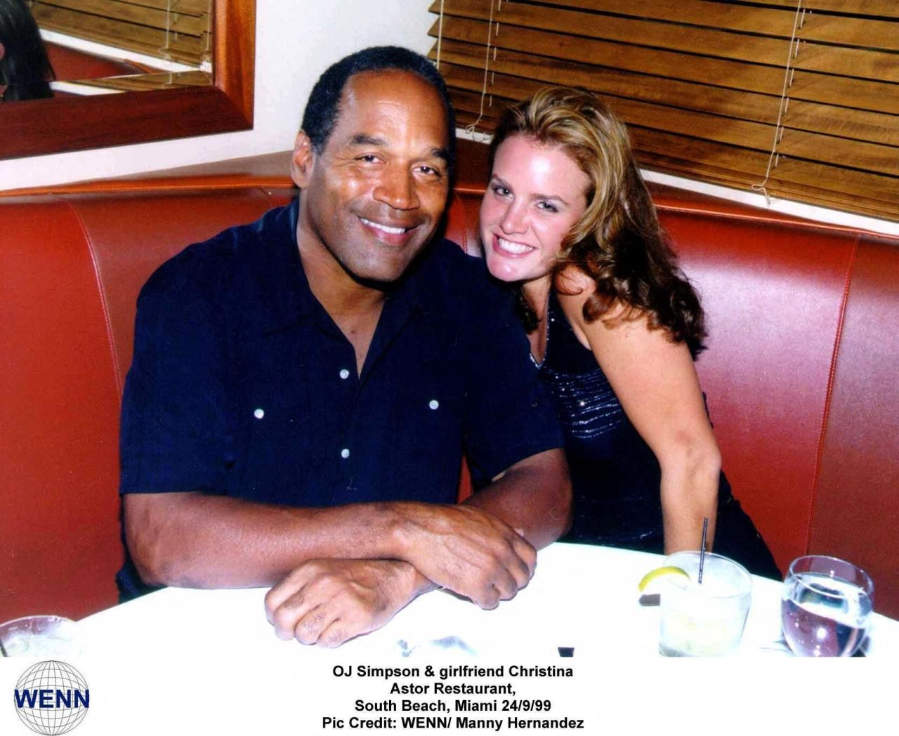 O.J. Simpson and his girlfriend Christina sitting together smiling in a restaurant booth with drinks on the table.