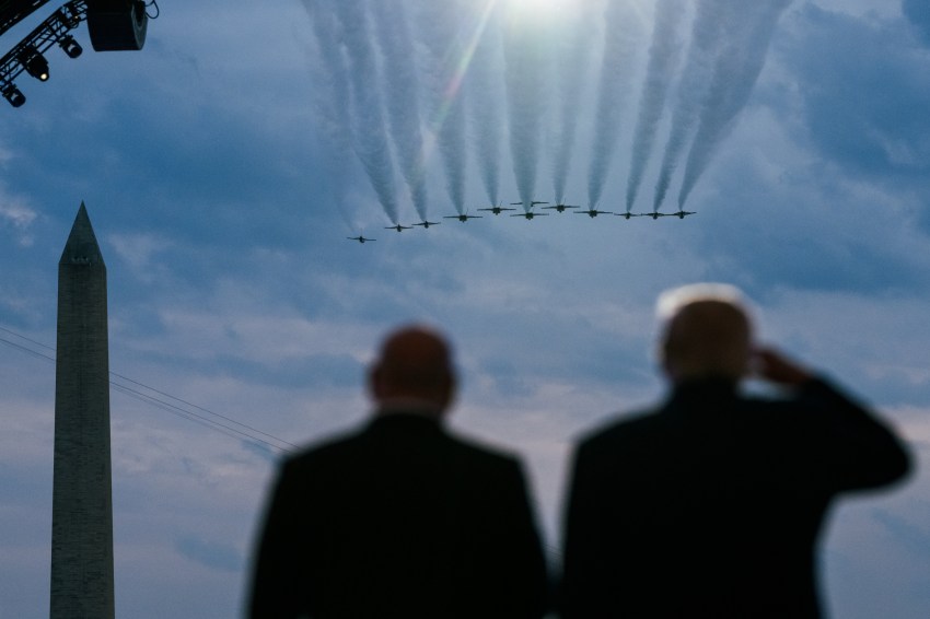 Two men seen from behind in silhouette watching a formation of jets with contrails fly over the Washington Monument.