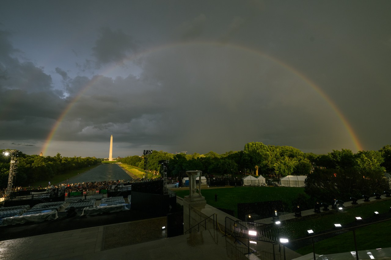 Vivid double rainbow spanning the sky above the Washington Monument and the White House South Lawn event setup at dusk.