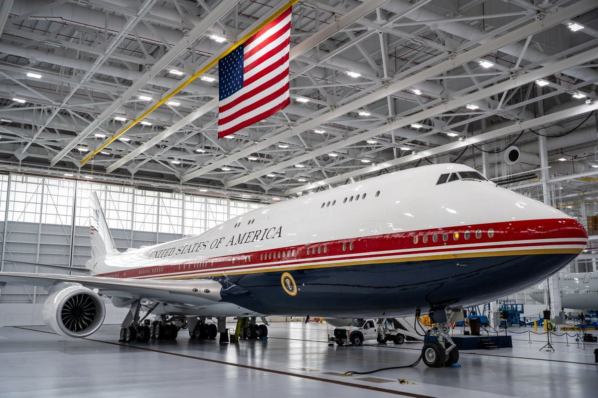 A large Boeing 747-8 aircraft painted in red, white, and blue with 'United States of America' on the fuselage inside a hangar at Joint Base Andrews.