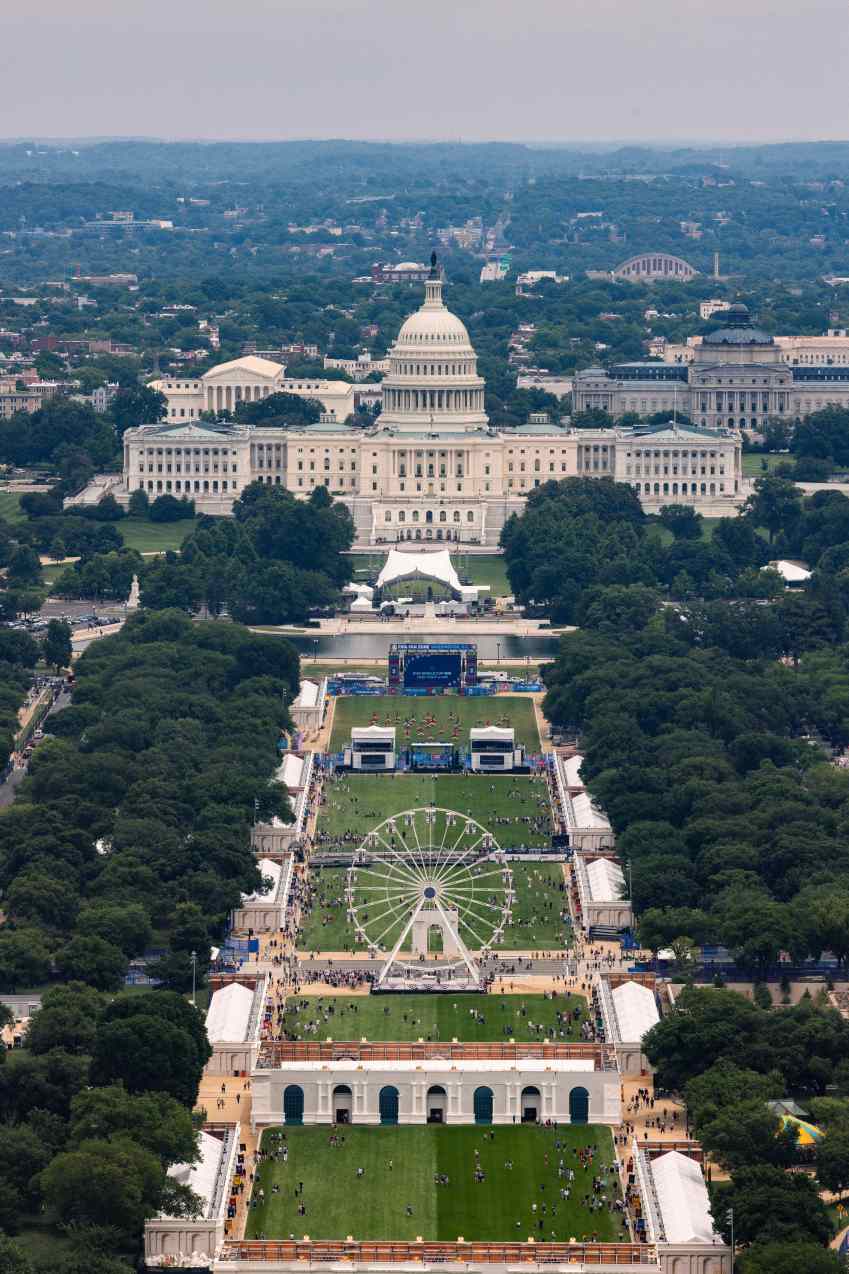 Aerial view of the Great American State Fair on the National Mall, with a large Ferris wheel in the foreground and the U.S. Capitol in the background